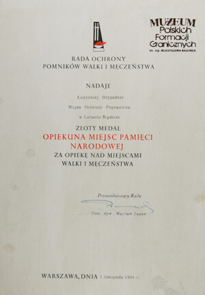 1. Tytuł: akt nadania złotego medalu „Opiekuna Miejsc Pamięci Narodowej”
2. Treść: nadanie Łużyckiej Brygadzie WOP złotego medalu Opiekuna Miejsc Pamięci Narodowej przez Przewodniczącego Rady Ochrony Pomników Walki i Męczeństwa gen. dyw. Wacława Jagasa w dniu 05.11.1984 r.
3. Hasło przedmiotowe: Wojska Ochrony Pogranicza, przedmioty pamiątkowe
4. Wytwórca: Rada Ochrony Pomników Walki i Męczeństwa
5. Czas powstania: 1984 r.
6. Miejsce sporządzenia: Polska, Warszawa
7. Materiał i technika wykonania: papier, druk 
8. Wymiary: 21 x 29,8 cm
9. Stan zachowania: dobry
10. Miejsce przechowywania/ właściciel: depozyt Sali Tradycji Ośrodka Szkoleń Specjalistycznych SG w Lubaniu