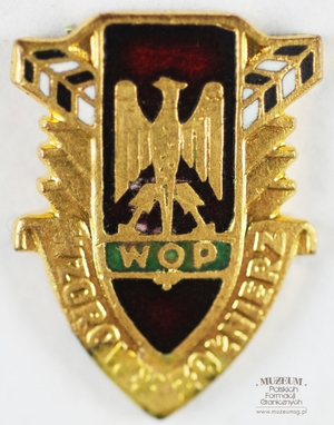 1.Nazwa własna: odznaka „Wzorowy Żołnierz” Wojsk Ochrony Pogranicza – miniaturka 
2.Charakterystyka przedmiotu: odznaka złota na szpilce, w kształcie tarczy z wizerunkiem orła (na czerwonym emaliowanym tle) trzymającego napis „WOP” (na zielonym emaliowanym tle). Tarcza u dołu obwiedziona napisem „Wzorowy Żołnierz”, u góry po bokach z dwóch stron, pod kątem 45 stopni wizerunki słupów granicznych (emaliowane na biało – czerwono). Wymiary: 1,5 cm x 1,9 cm
3.Czas powstania: przed 1991 r. 
4.Hasła przedmiotowe: Wojska Ochrony Pogranicza, odznaczenia
5.Miejsce przechowywania/ właściciel: Sala Tradycji Ośrodka Szkoleń Specjalistycznych SG w Lubaniu. Odznakę użyczył  pan Paweł Żółtański