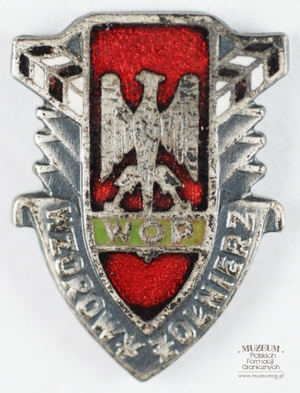 1.Nazwa własna: odznaka „Wzorowy Żołnierz” Wojsk Ochrony Pogranicza – miniaturka 
2.Charakterystyka przedmiotu: odznaka srebrna na szpilce, w kształcie tarczy z wizerunkiem orła (na czerwonym emaliowanym tle) trzymającego napis „WOP” (na zielonym emaliowanym tle). Tarcza u dołu obwiedziona napisem „Wzorowy Żołnierz”, u góry po bokach z dwóch stron, pod kątem 45 stopni wizerunki słupów granicznych (emaliowane na biało – czerwono). Wymiary: 1,5 cm x 1,9 cm
3.Czas powstania: przed 1991 r. 
4.Hasła przedmiotowe: Wojska Ochrony Pogranicza, odznaczenia
5.Miejsce przechowywania/ właściciel: Sala Tradycji Ośrodka Szkoleń Specjalistycznych SG w Lubaniu. Odznakę użyczył  pan Paweł Żółtański